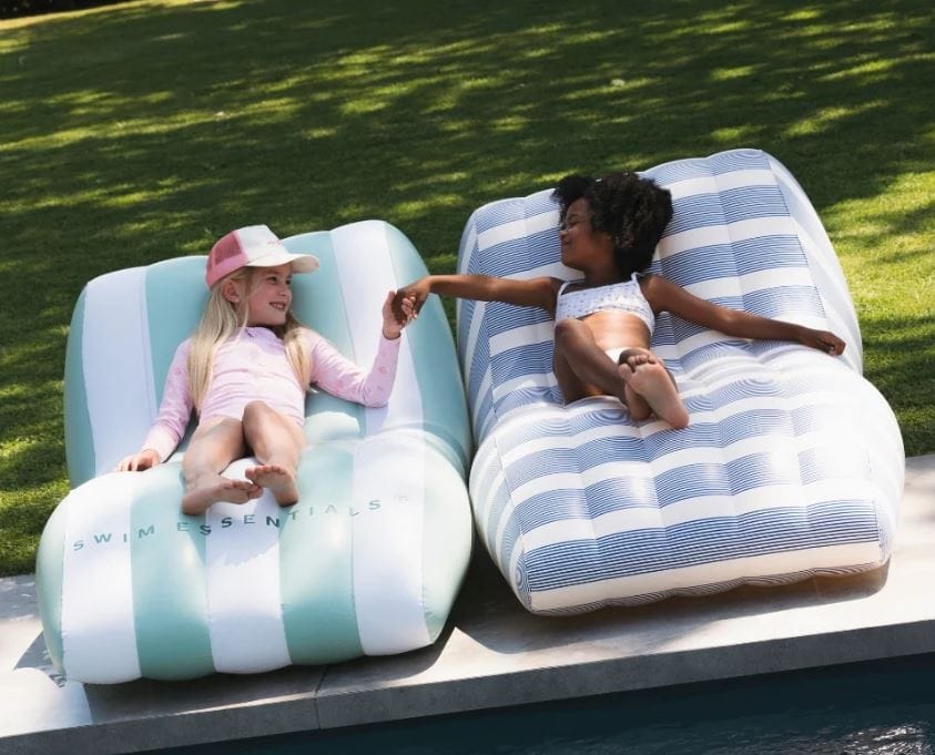 Twee meisjes ontspannen op opblaasbare ligstoelen bij zwembad